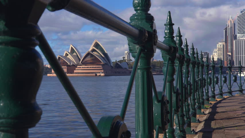 Close-up shot along the historic-style waterfront railing with the Sydney Opera House and city buildings visible across the water. Sydney, New South Wales, Australia.