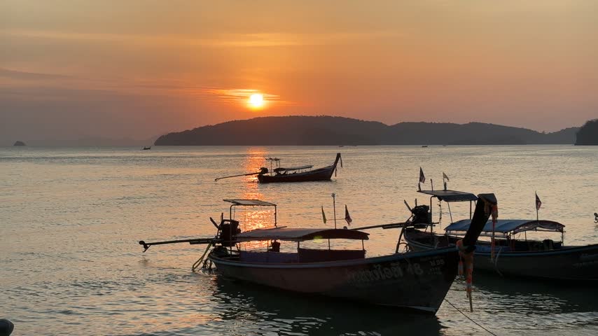 Longtail boats on the water at sunset in Krabi Thailand with a scenic horizon