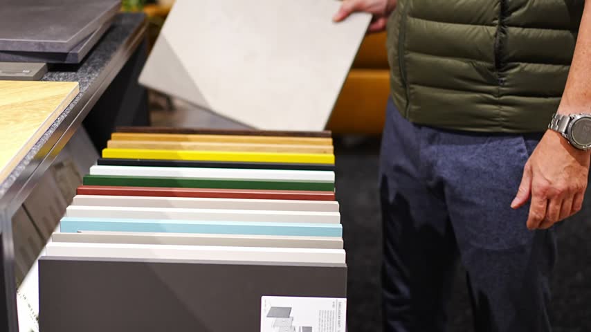 Man browses cabinet door samples in furniture showroom. Choosing colors and finishes for kitchen renovation with selective focus and soft background.