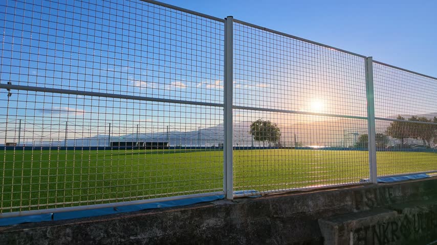 Video of an outdoor football field behind a tall protective fence during golden hour