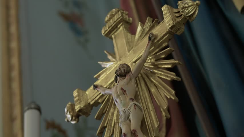A carved crucifix with a painted figure of Jesus on a gilded cross with golden rays hangs inside a Catholic church.