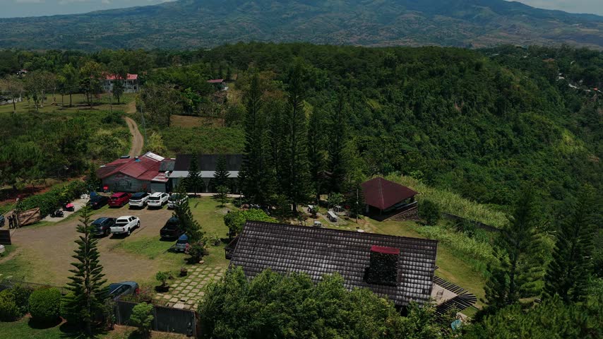 Aerial view of hillside cafe with parked cars and lush greenery, Mount Kanlaon beyond