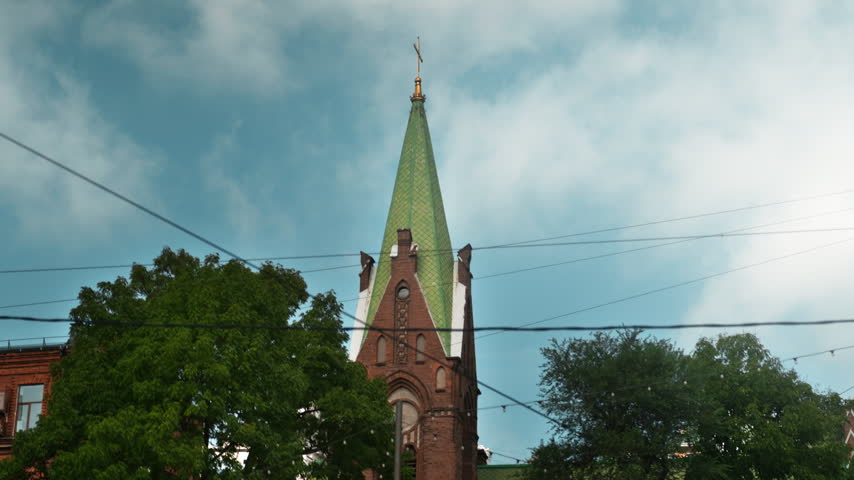 A red-brick Gothic church with a green roof stands in the middle of the city. Religion and culture.