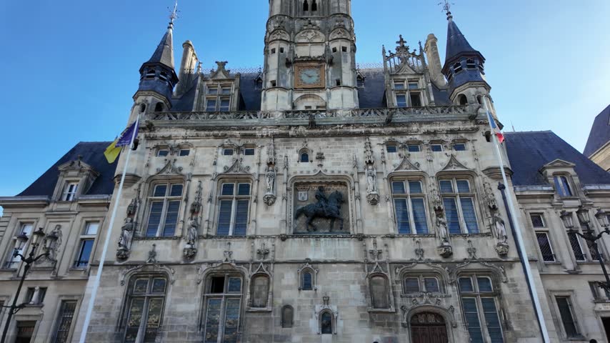 Front view of Compiègne Town Hall featuring ornate stone carvings, Gothic windows, statues, turrets, a central tower and an equestrian sculpture