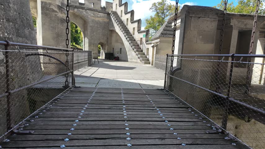 Slow motion movement across the wooden drawbridge at Château de Pierrefonds, showing suspension chains, stone fortifications and an interior courtyard