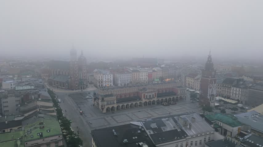 Aerial perspective capturing the famous historic Main Market Square in Krakow, Poland, enveloped in a thick layer of fog, highlighting the majestic towers of St. Mary