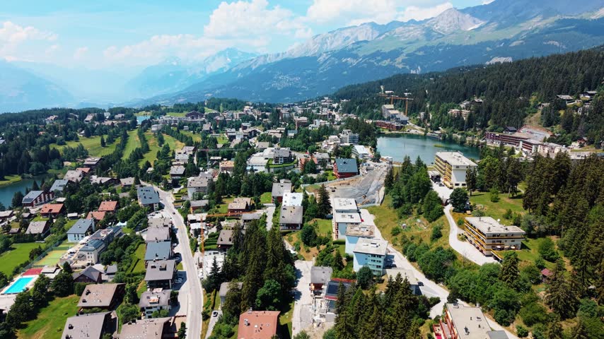 Rooftops skim past as the drone flies low toward Lac Grenon in Crans-Montana.
