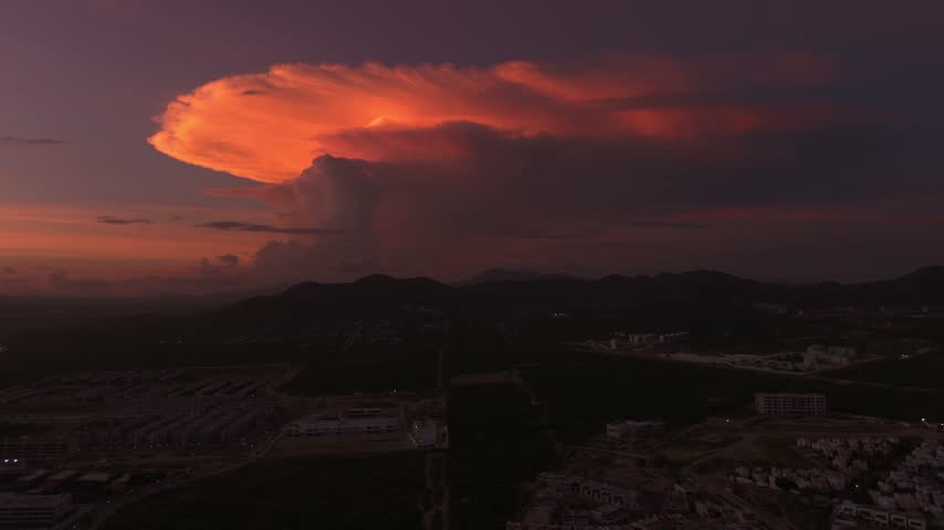 Stunning aerial hyperlapse of a massive colorful storm cloud over the green mountains and cityscape of Cabo San Lucas at dusk.