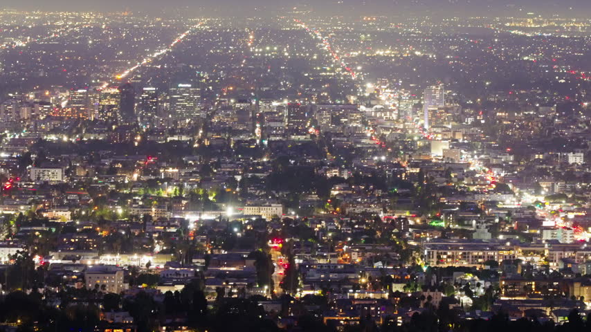 The Los Angeles skyline shines beneath the dark evening sky as countless city lights illuminate the urban landscape, creating a vibrant California panorama filled with nighttime atmosphere.