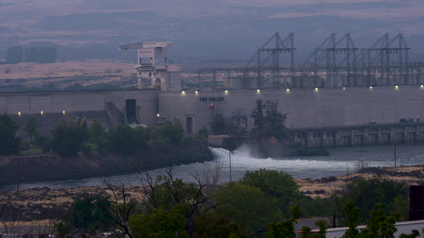 The Dalles Dam on the Columbia River in Oregon, with water flowing through the hydroelectric facility as wildfire smoke blankets the surrounding landscape.