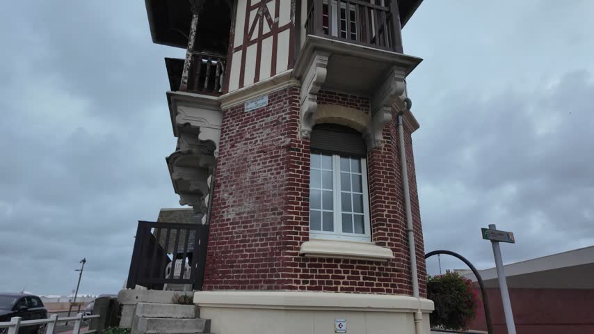 Street view of a historic seaside house in Mers-les-Bains featuring red brick, half-timbered upper walls, a projecting balcony and ornate architectural details