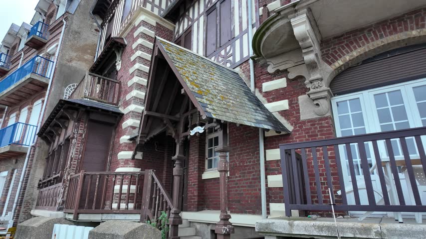Street view of a historic seaside house in Mers-les-Bains featuring red brick, half-timbered details, carved woodwork, balconies and a covered entrance
