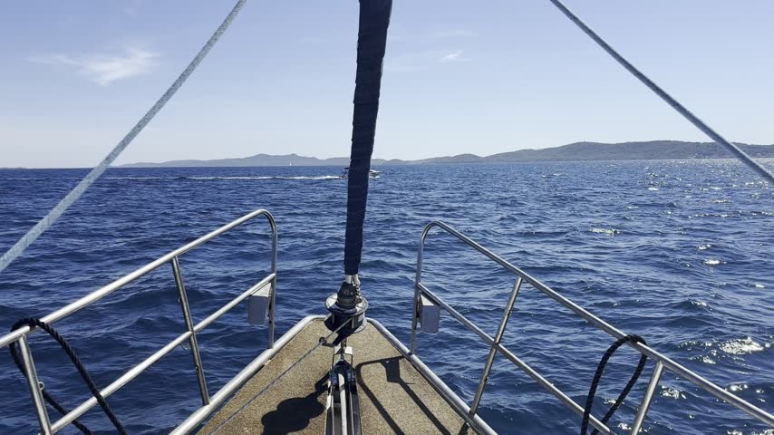 Another boat crosses in front of a sailboat while cruising across the blue sea near a distant coastline.
