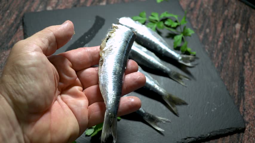 Male hand holds a raw fresh sardine.