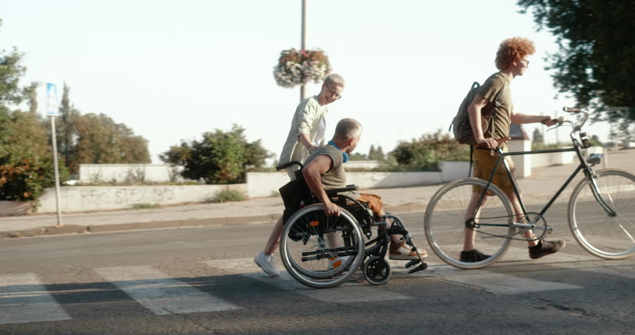 Group of friends including a young man in a wheelchair cross a pedestrian crossing together in the city, showing friendship, inclusion and active urban life.