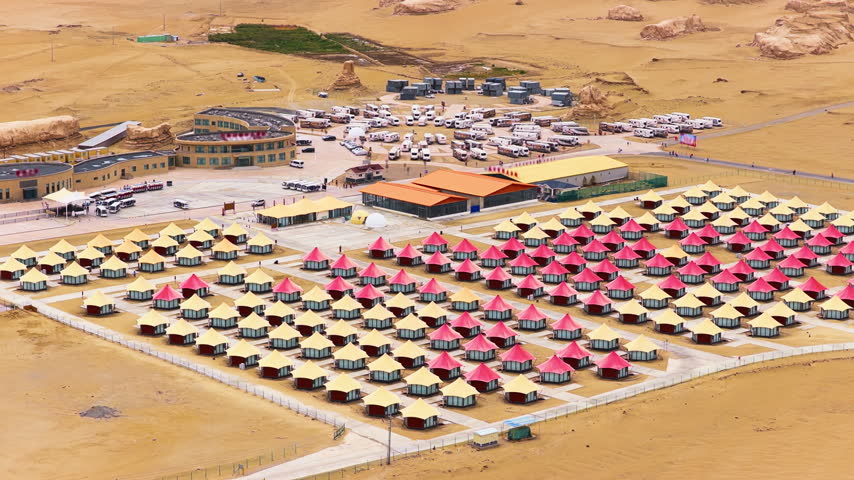 High-angle shot displays a desert glamping resort with rows of red and beige luxury tents near RV parking.