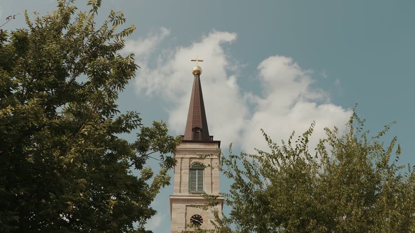 Historic Church Steeple with Cross Framed by Trees Under a Blue Sky