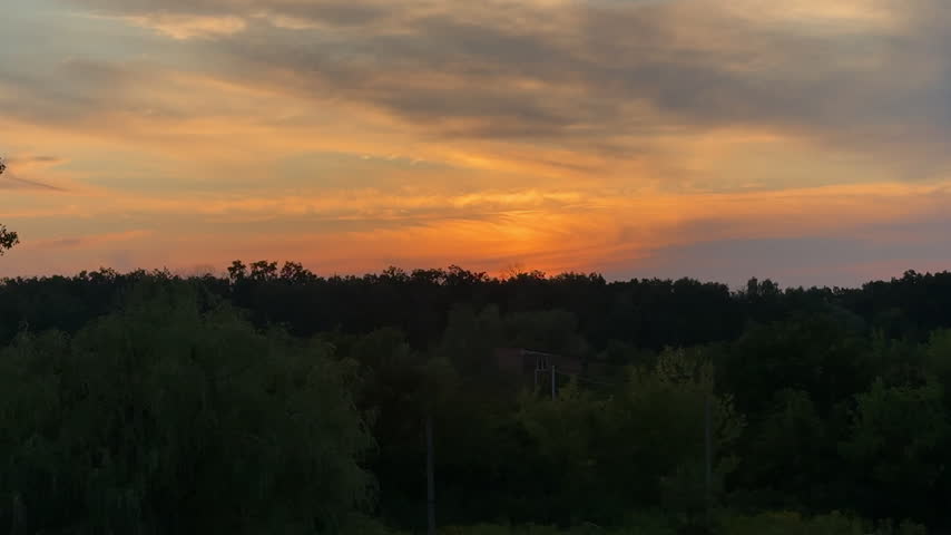 Scenic Golden Hour Sunset Over Dark Forest Silhouette with Vibrant Orange and Yellow Clouds