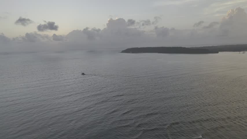 Aerial drone view of a ship sailing across the Arabian Sea near Miramar Beach, Goa, with a glowing sunset behind monsoon clouds and a dramatic cliff silhouette.