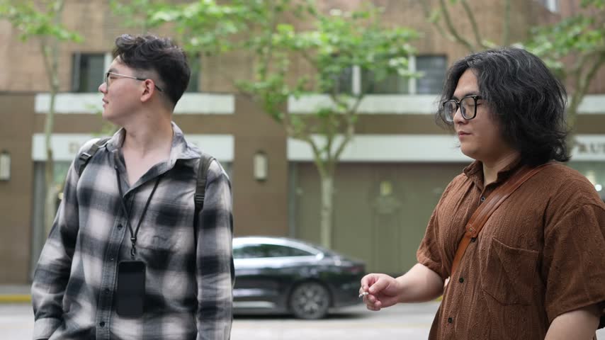 A man in a plaid shirt looks upward while standing on a tree lined urban street.