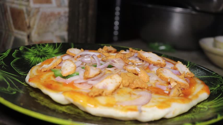 Homemade chicken pizza with cheese and onion toppings on a plate.
