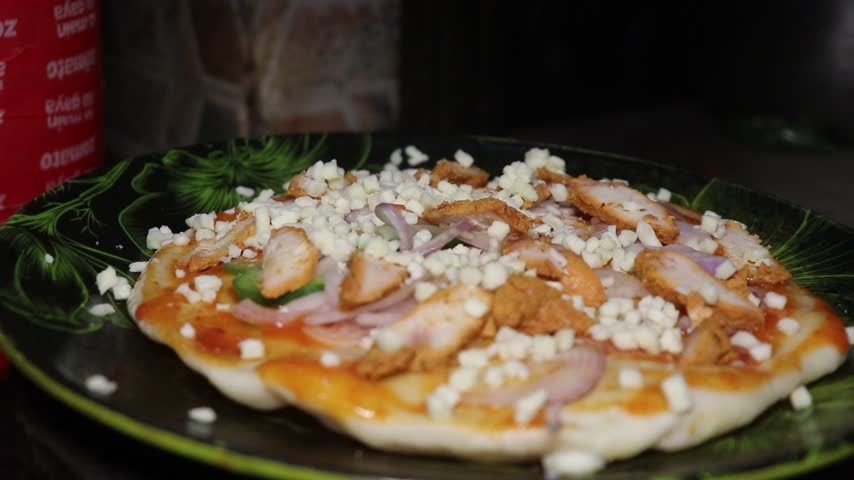 Homemade chicken pizza with cheese and onion toppings on a plate.