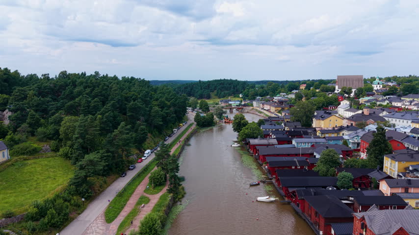 Aerial view of Porvoo, Finland, showing the Porvoonjoki river, iconic red riverside warehouses, colorful old town buildings, and lush green forest in summer