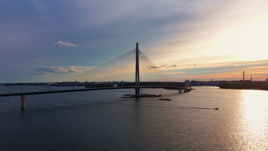 Kruunuvuorensilta cable-stayed bridge spanning the sea bay in Helsinki, Finland, with boats passing beneath and warm sunset sky over the city skyline