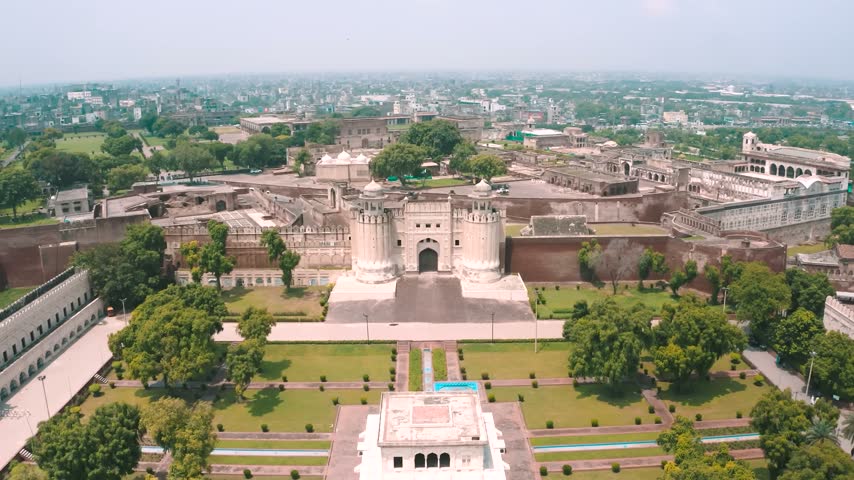 A wide-angle drone view capturing the majestic Alamgiri Gate, the defensive fortification walls of the UNESCO-listed Lahore Fort, and the surrounding urban sprawl of Lahore, Pakistan.