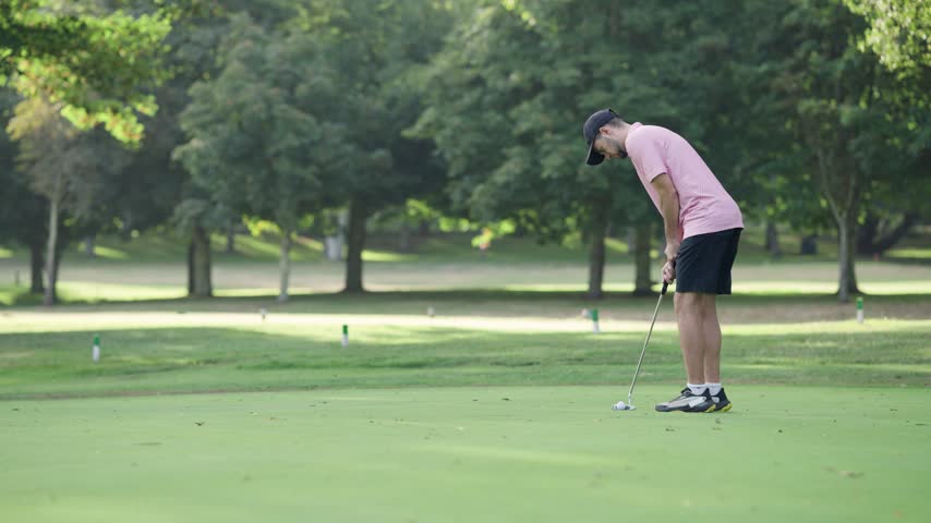 Professional golfer on the green concentrating and hitting the ball with a putter. Man playing a game of golf during a tournament