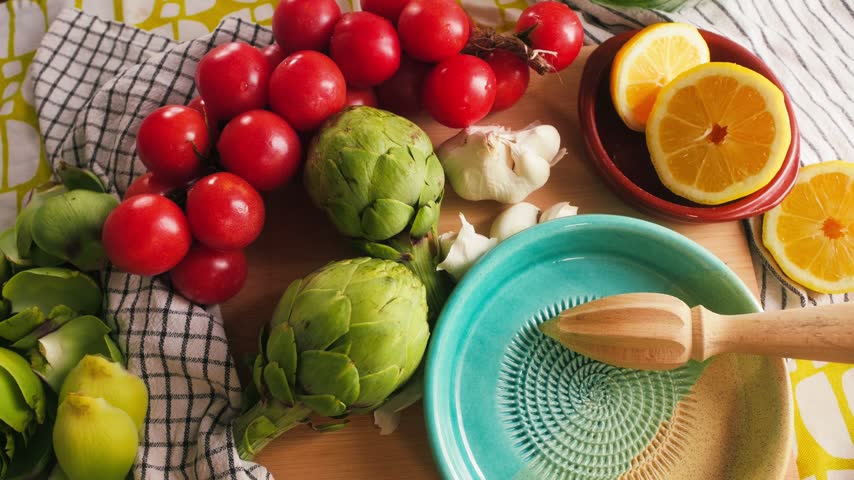 Fresh tomatoes, artichokes, garlic and lemon arranged on a kitchen table before cooking. Natural ingredients for Mediterranean cuisine.