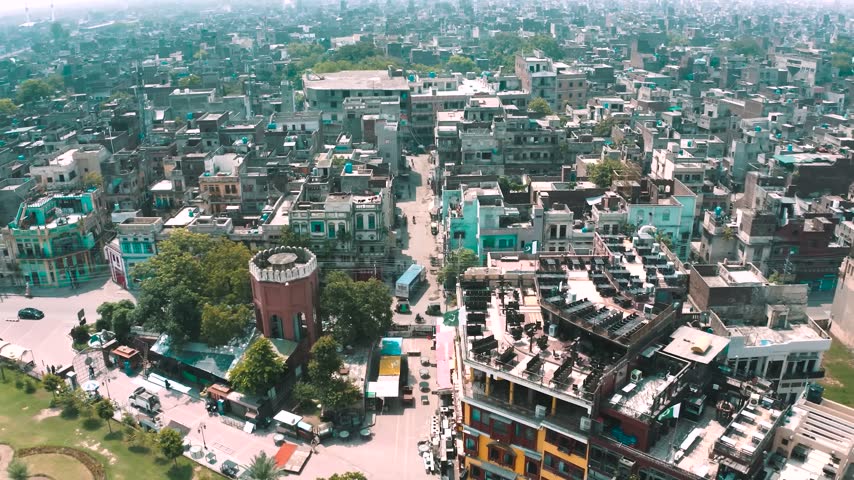 High-angle aerial panorama looking down at the colorful buildings, rooftop open-air restaurants, and the iconic historic brick water tower at the entrance of Fort Road Food Street in Lahore, Pakistan.