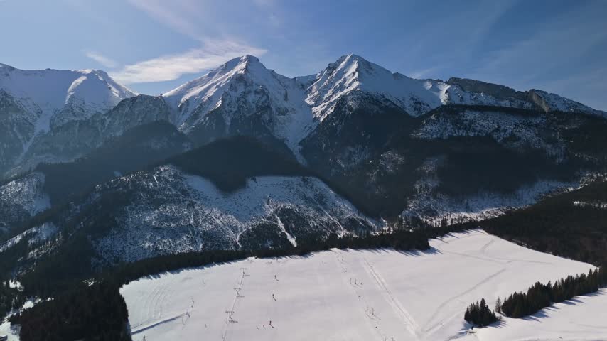 Ždiar ski resort in the High Tatras, Slovakia, with snowy ski slopes, chairlifts, pine forests and mountain peaks in winter, captured by drone over the alpine landscape.