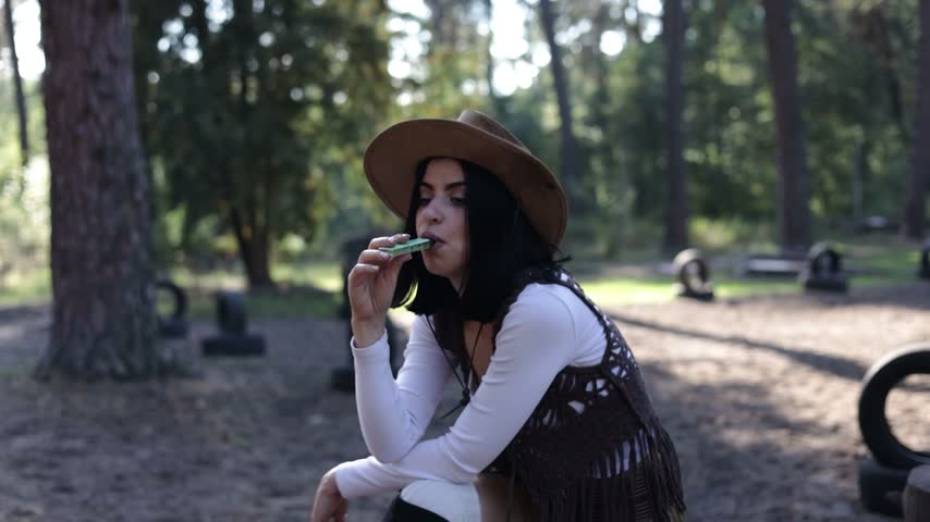 Beautiful young girl model in a cowboy hat blows smoke from her mouth using an electronic cigarette. Health risks of tobacco, addiction. 