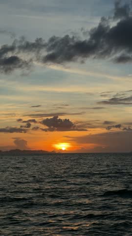 The sun sets over the ocean, casting different colors across the sky and water as daylight fades into evening.