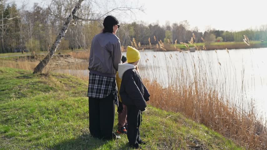 Parent and child standing near lakeshore with gulls in flight under warm autumn afternoon light, calm water reflections, and quiet outdoor nature