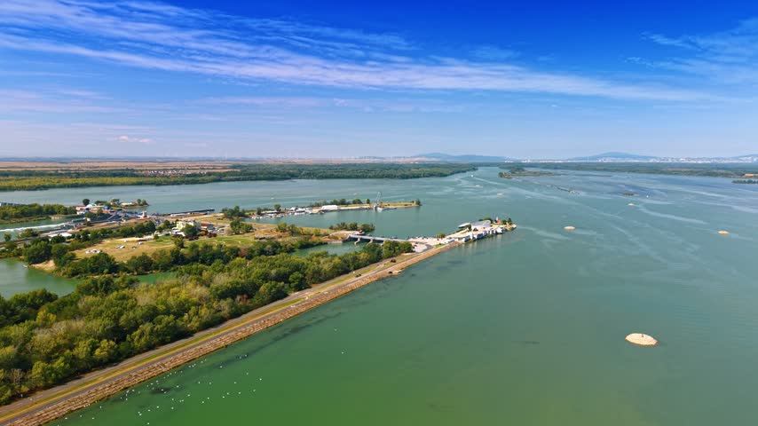 Small harbor facility on water shore. Aerial perspective shows dock structures and buildings situated on green reservoir bank.