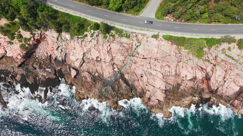 Directly overhead aerial view of waves breaking on the pink granite coastline beside the Park Loop Road in Acadia National Park, Maine, USA.