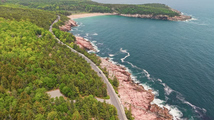 Aerial view of Sand Beach, a turquoise cove framed by pink granite headlands and forest in Acadia National Park, Maine, USA.