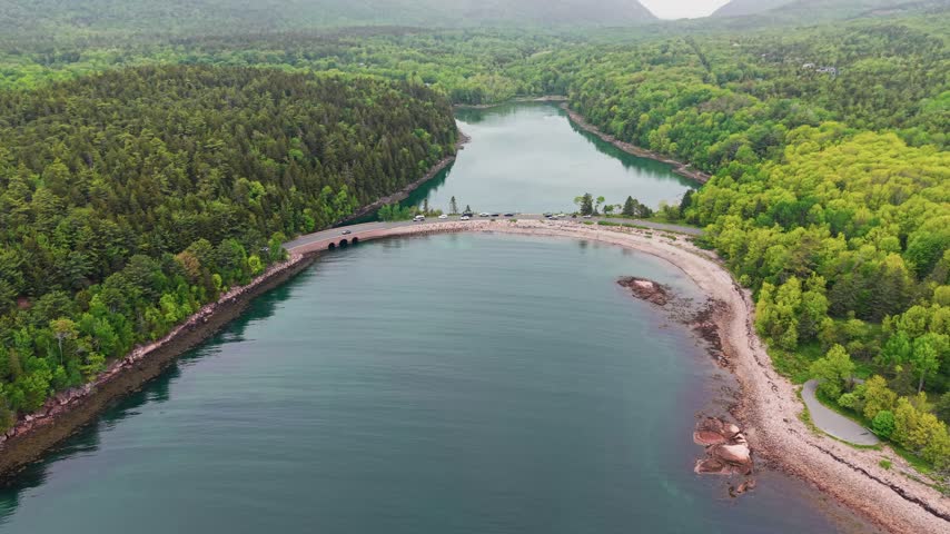 Aerial view of the historic Otter Cove stone bridge and causeway crossing a tidal cove surrounded by forest in Acadia National Park, Maine, USA.