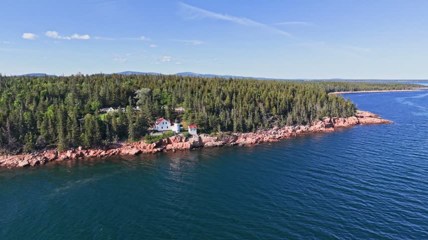 Orbiting aerial view of Bass Harbor Head Lighthouse among spruce trees on the rugged coast of Acadia National Park, Maine, USA.