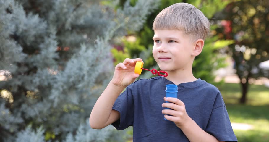Cute little boy blowing soap bubbles outdoors