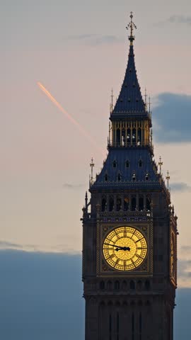Iconic Elizabeth tower at dusk showing glowing clock face and faint jet stream trail in evening sky cinematic video clip.