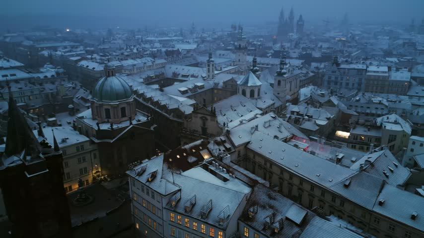 Cinematic drone footage capturing beautiful snowy architecture in historical Prague center under gloomy winter evening sky.