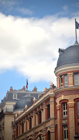 French national flag fluttering above architectural dome of classic Parisian building under white clouds and blue sky.