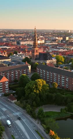 Dynamic drone flight over Christianshavn district showing historic church spire and urban architecture at sunset.