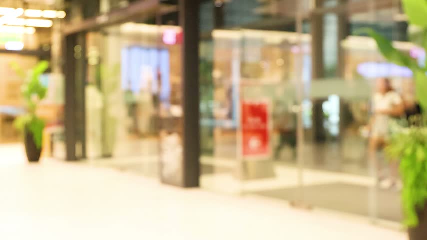 Blurred motion of people walking through bright modern shopping mall corridor during daytime. Cinematic footage capturing everyday urban retail life in motion.