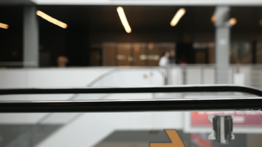 Close-up of several people riding a moving escalator inside a modern public building, showing everyday urban mobility, transportation and pedestrian movement.