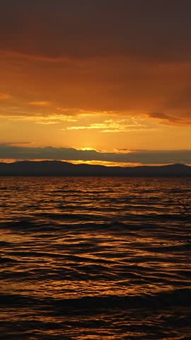 A very beautiful sunset landscape with views of the lake and mountains. The golden hour. The mirror image of sunset colors on the water. Unique natural beauty. Vertical video.