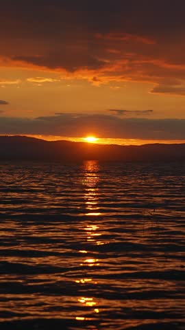 A very beautiful sunset landscape with views of the lake and mountains. The golden hour. The mirror image of sunset colors on the water. Unique natural beauty. Vertical video.